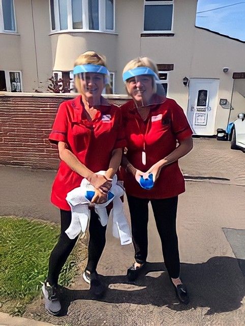 Two crossroads workers outside a home wearing face shields 
